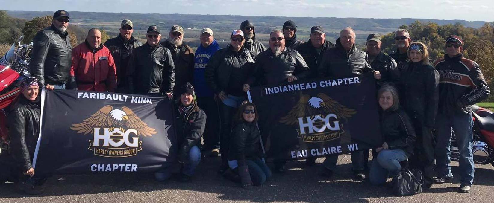 A group of members wearing riding gear stand behind a HOG banner.